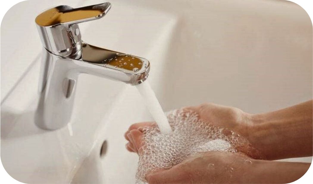 Ruke pod mlazom vode iz moderne baterije za kupatilo u svakodnevnoj upotrebi.