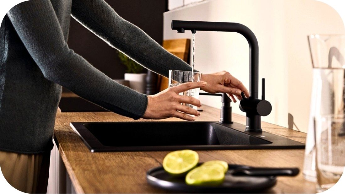 Moderna crna kuhinjska slavina tokom sipanja vode u čašu Moderna crna kuhinjska slavina tokom sipanja vode u čašu