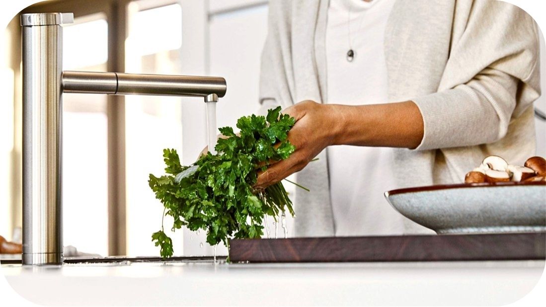 Ruke koje ispiraju peršun ispod moderne kuhinjske slavine od nerđajućeg čelika