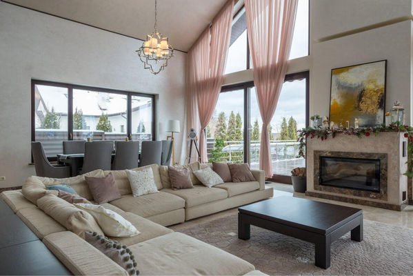 Prostran dnevni boravak sa modernim kaminom, panoramskim prozorima, pastelno bež sofom i dekoracijama za toplu atmosferu.